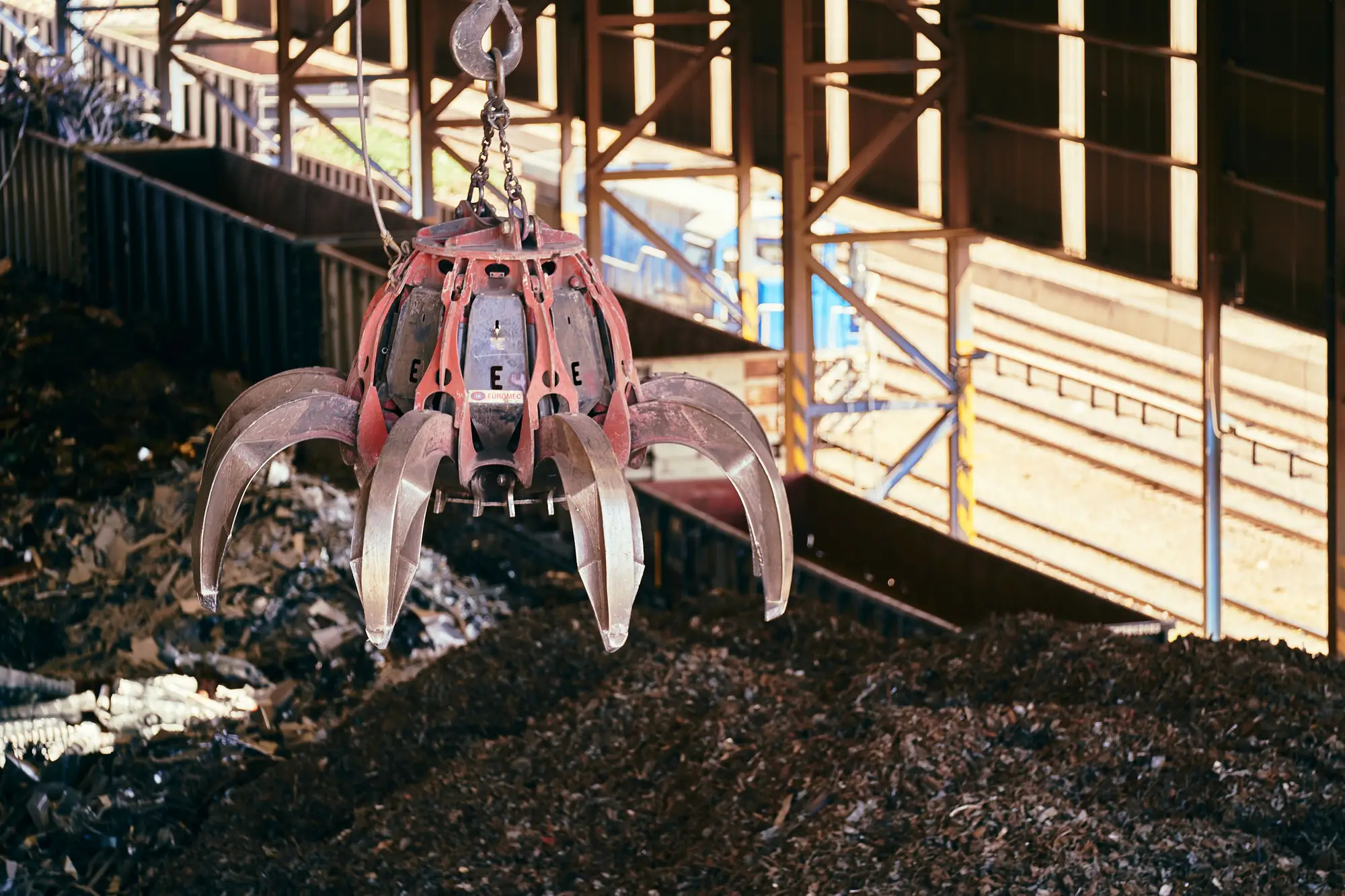 A grapple hanging over a heap of shredded scrap inside a steel-framed shed